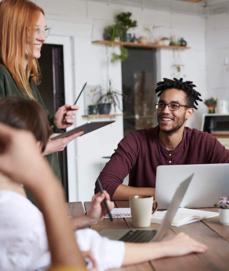 Smiling team having a casual discussion at a wooden table with laptops and coffee