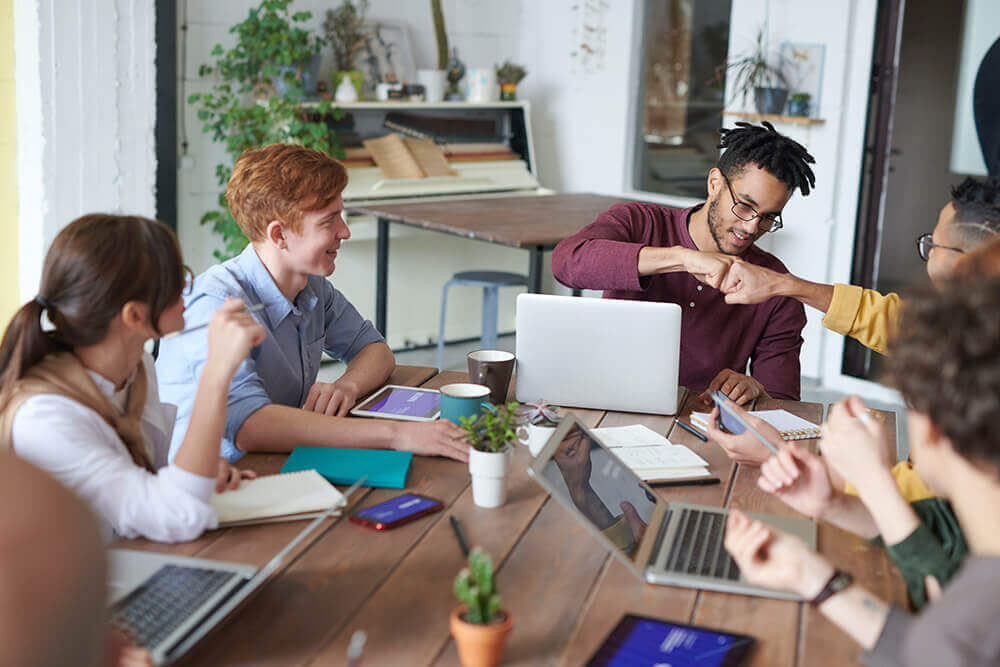 A group of people sitting around a table with laptops, focusing on NEW projects.