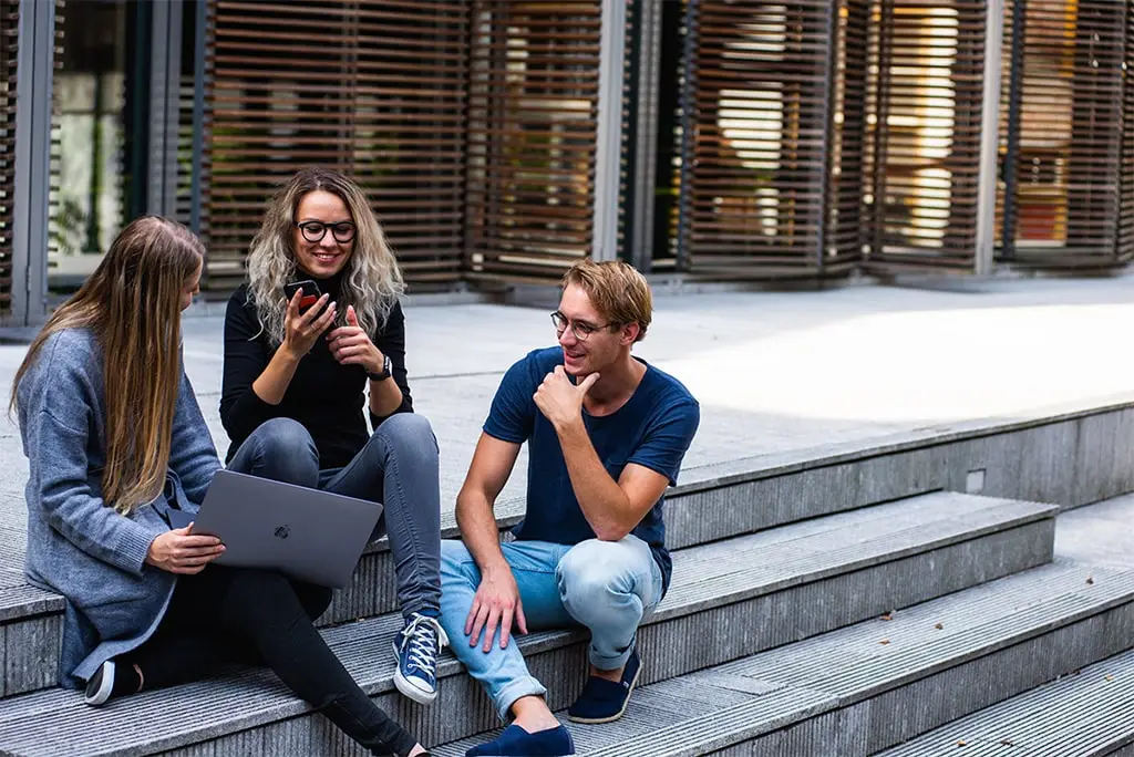 Group of young adults sitting on stairs using a laptop and smartphone together