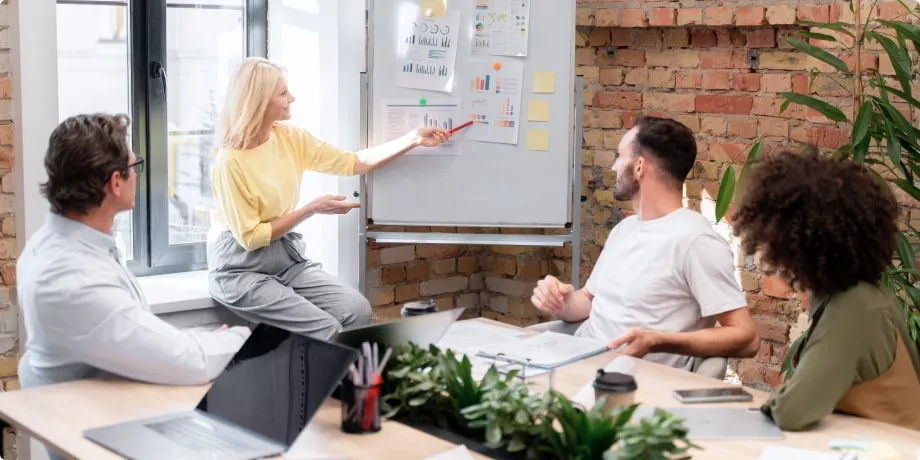 Team collaborating in a modern office while a woman presents marketing data on a whiteboard.