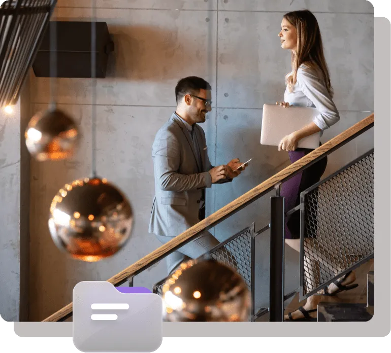 Two professionals walking upstairs in a modern office setting, holding devices and laptops