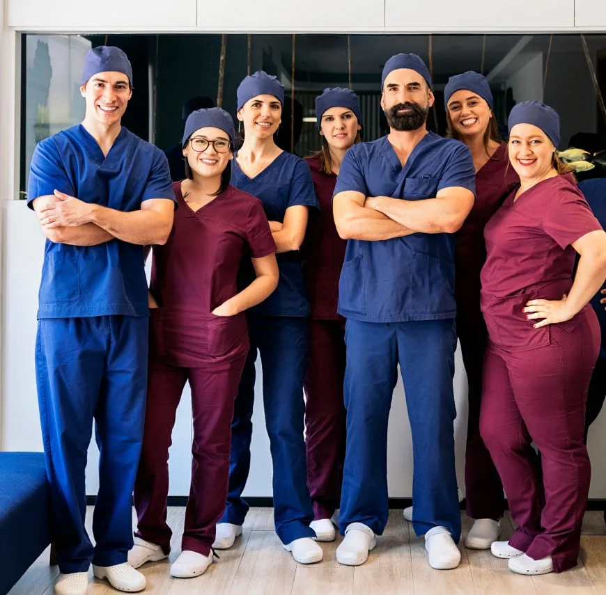 Group of professional dentists in scrubs smiling and posing together at a dental clinic.