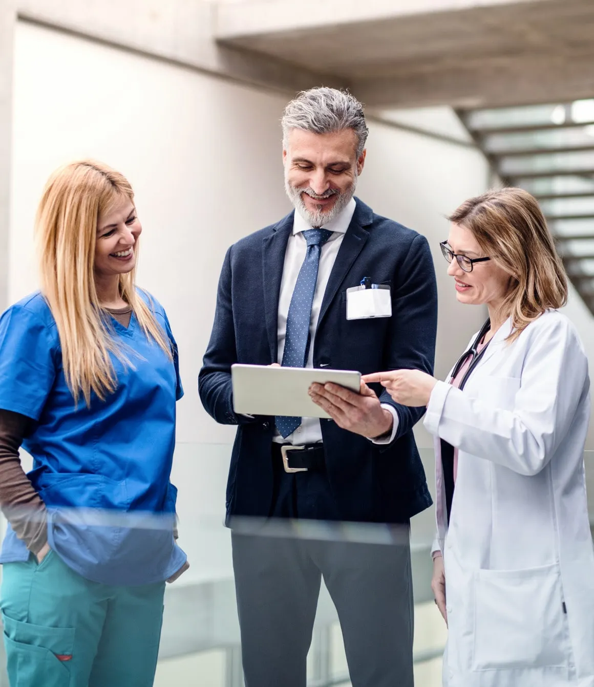 Medical professionals and an executive discussing information on a digital tablet in a hospital or healthcare facility.
