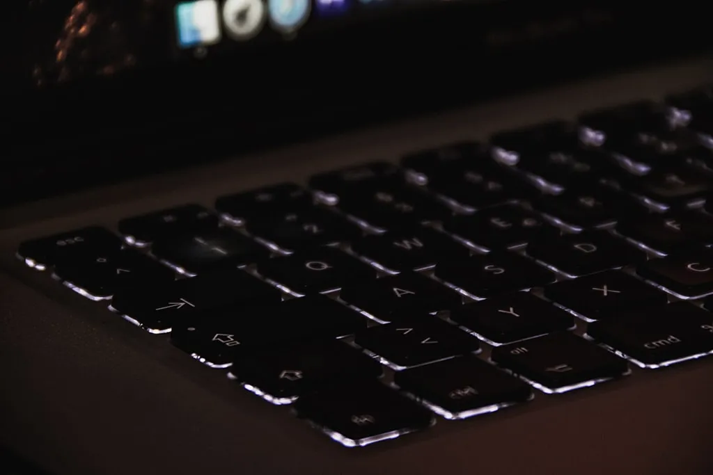 Close-up of illuminated MacBook keyboard in low light showing backlit keys.