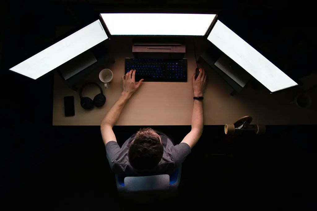 Top view of a person working on a triple-monitor computer setup in a dark room.