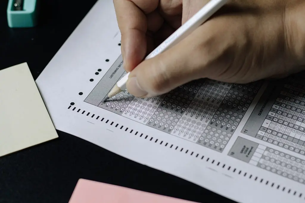 Close-up of a person filling out a multiple-choice answer sheet using a pencil during an exam.
