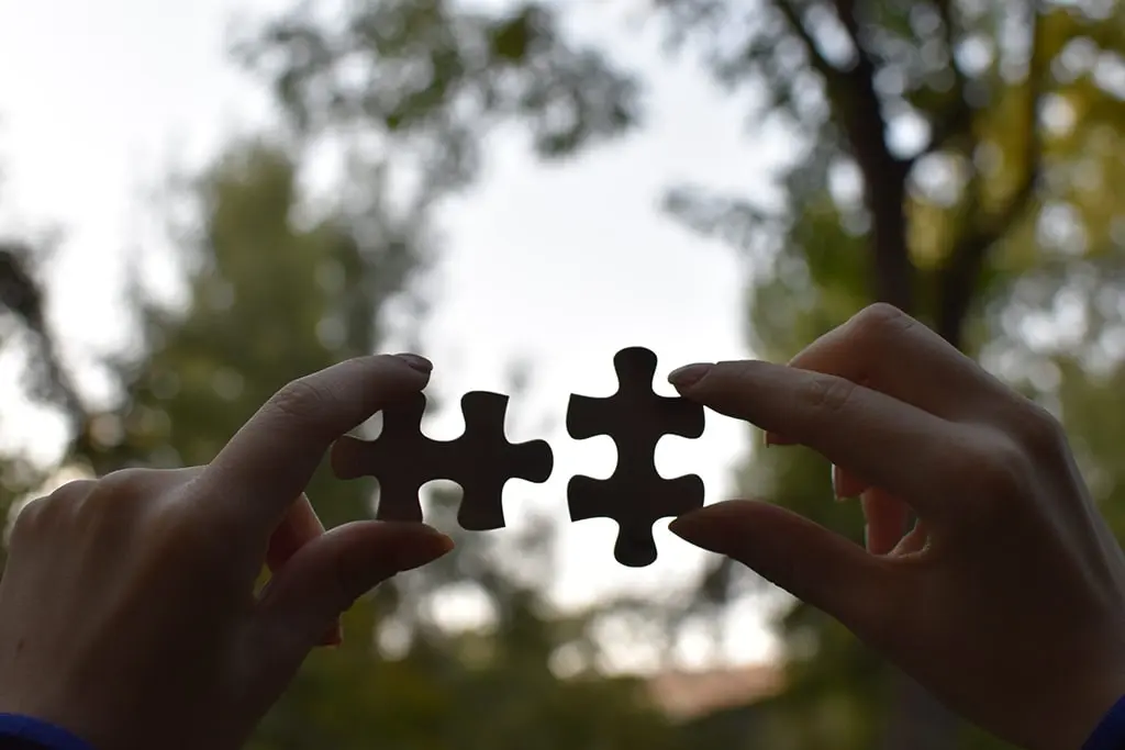 Two hands holding matching puzzle pieces outdoors, symbolizing connection and teamwork.