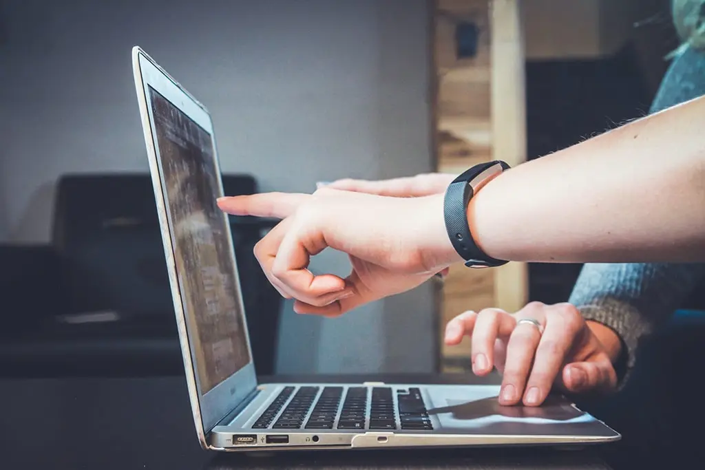 Two people collaborating by pointing at a laptop screen, discussing content or design together.