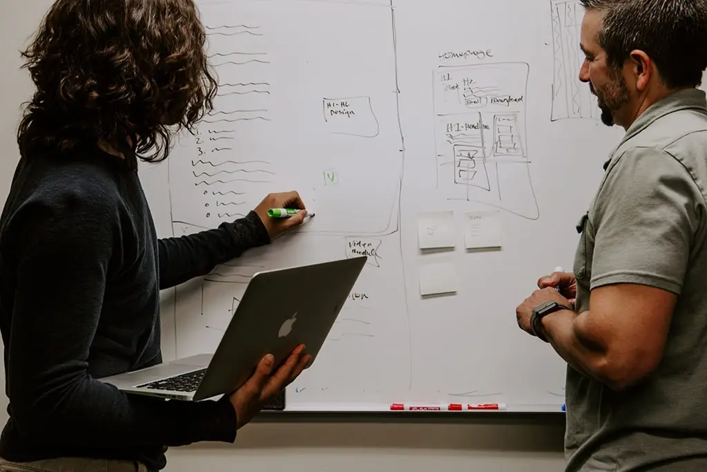 Two team members discussing website layout and content strategy while sketching wireframes on a whiteboard.
