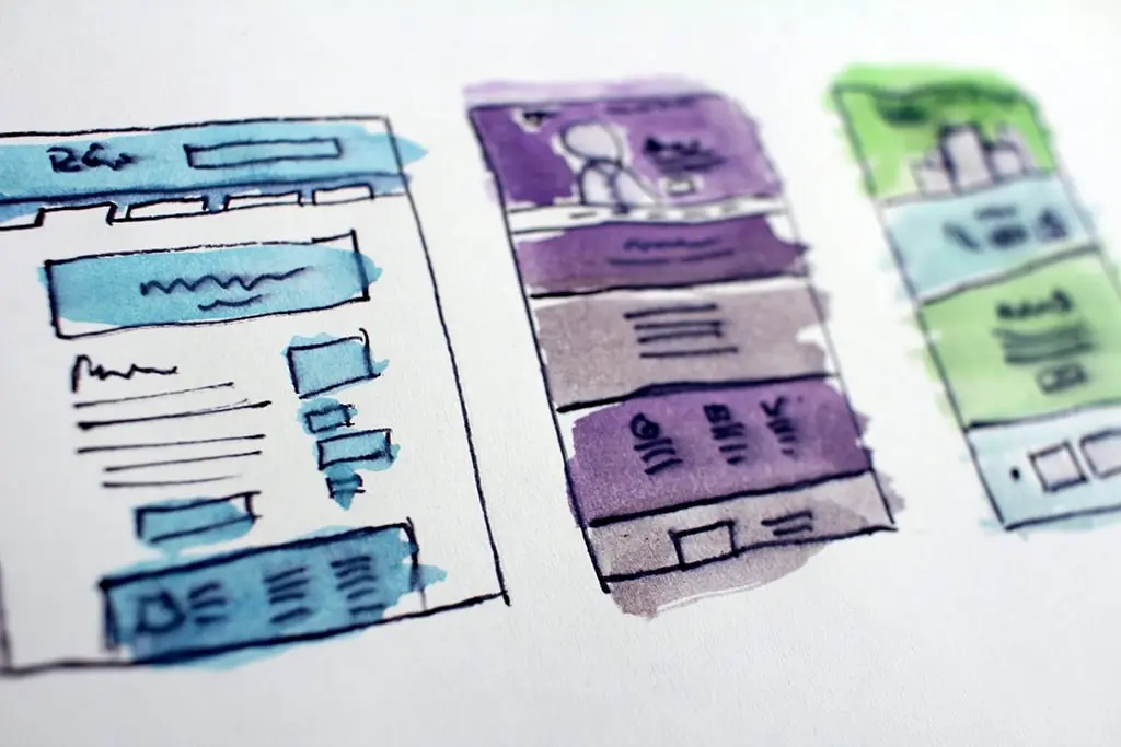 Hand-drawn website wireframes with colorful highlights showing different layout designs on paper.