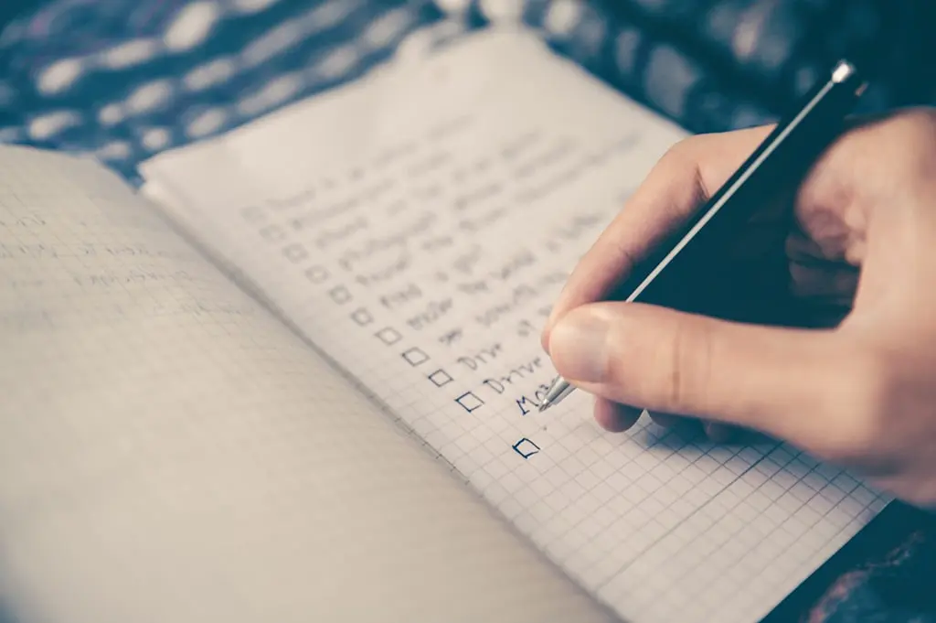 Close-up of a hand writing a checklist in a squared notebook with a pen.