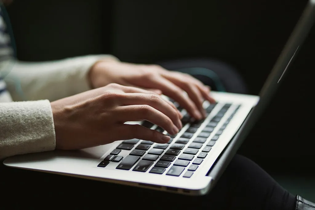 Close-up of hands typing on a laptop keyboard in a dimly lit setting