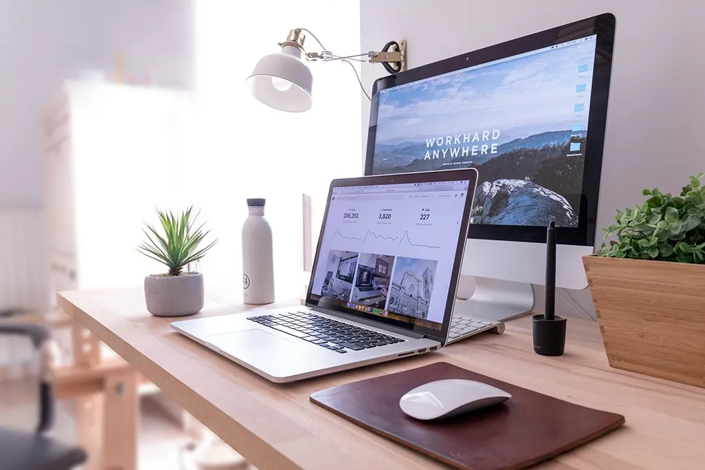 Minimal creative home office desk with laptop, iMac, potted plants, and a water bottle.