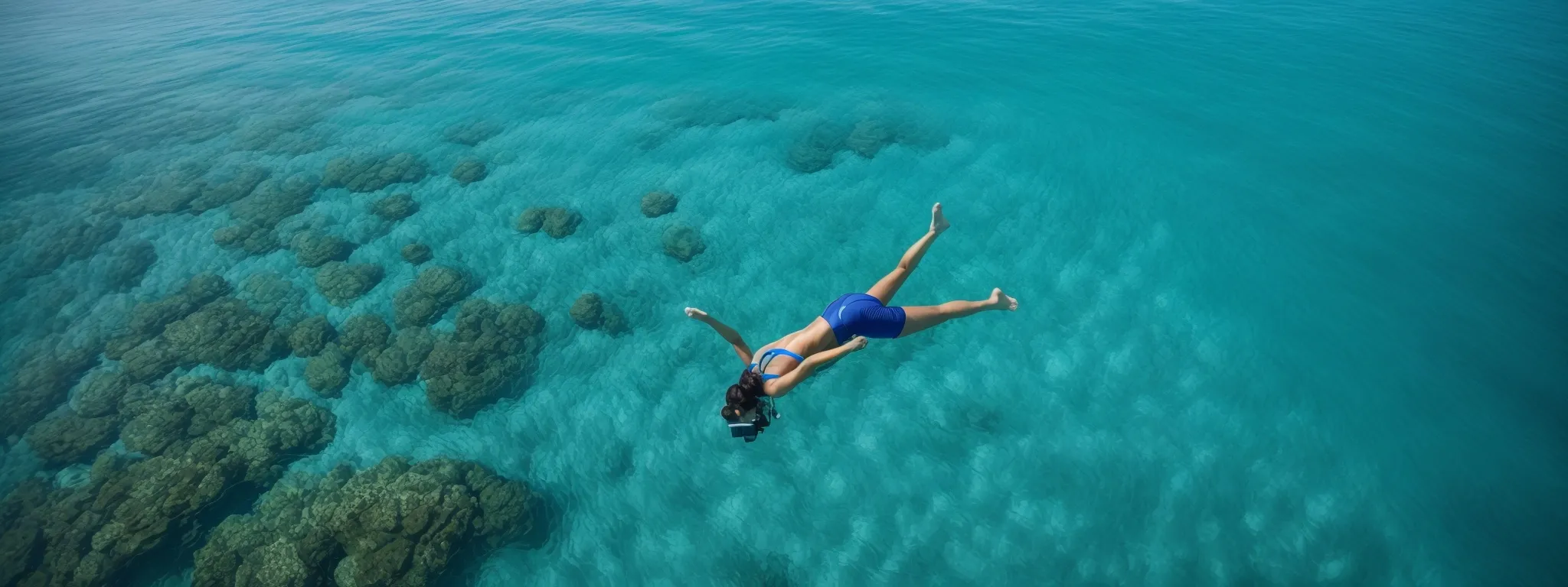 A person in blue swimwear snorkels face down above coral reefs in clear, turquoise ocean water.