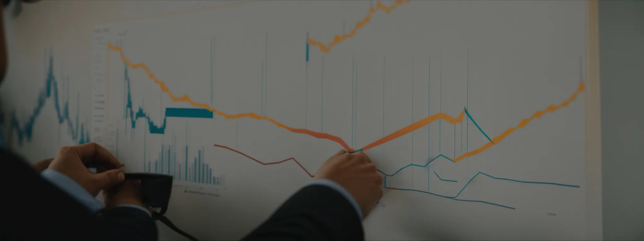 Person pointing at a large chart with multiple colored lines and bar graphs, showing data trends and fluctuations.