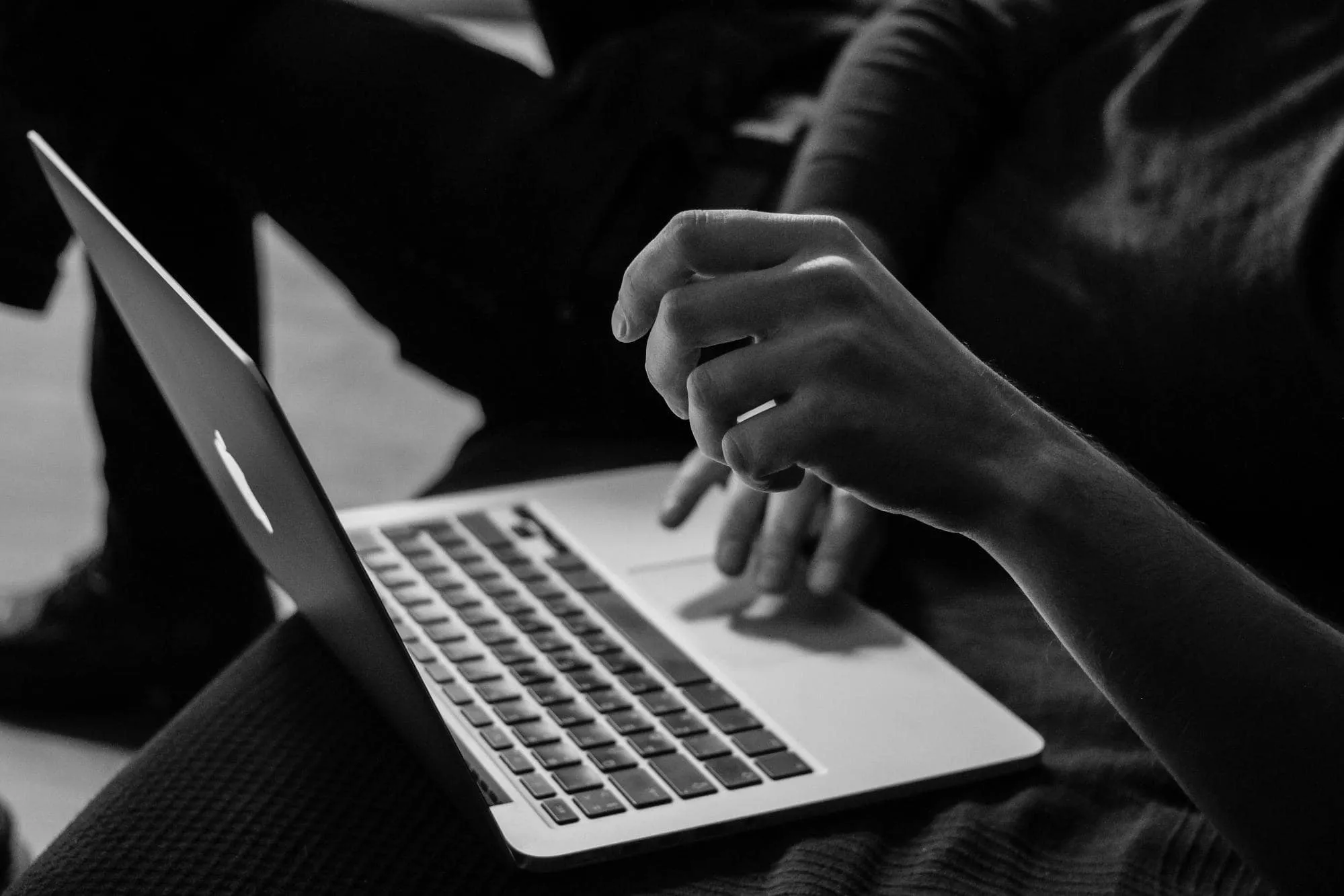 Black and white close-up of a person working on a laptop, focusing on hands using the keyboard and trackpad