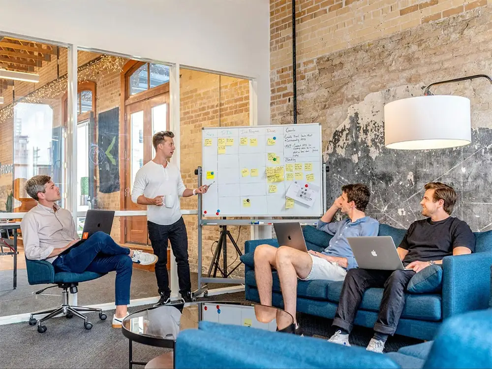 Team strategizing with laptops and a whiteboard, discussing how to track PR success and optimize campaign performance in a modern office setting