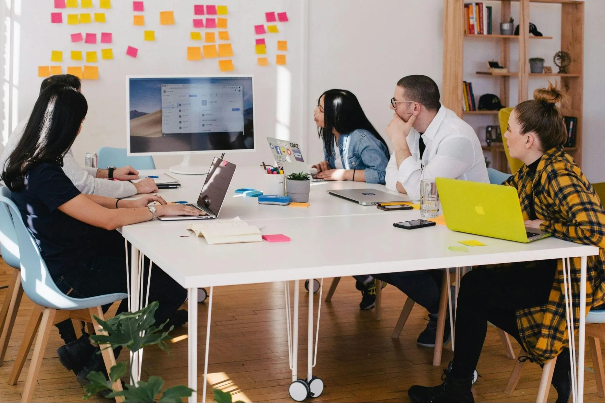 Team of professionals collaborating in a modern office, using laptops and digital tools during a brainstorming meeting with sticky notes on the wall