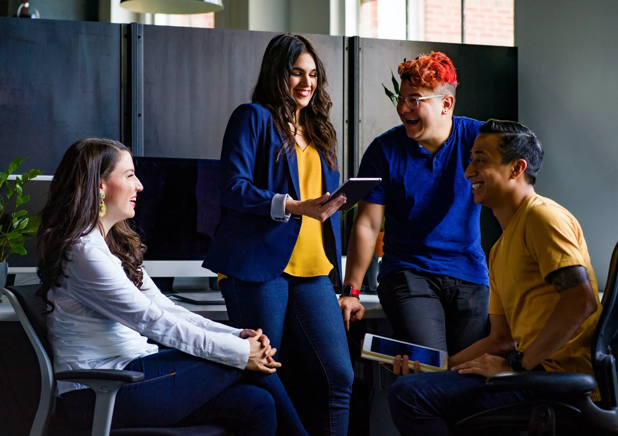 Diverse group of colleagues having a lively discussion in a modern office, holding tablets and smiling during a team meeting