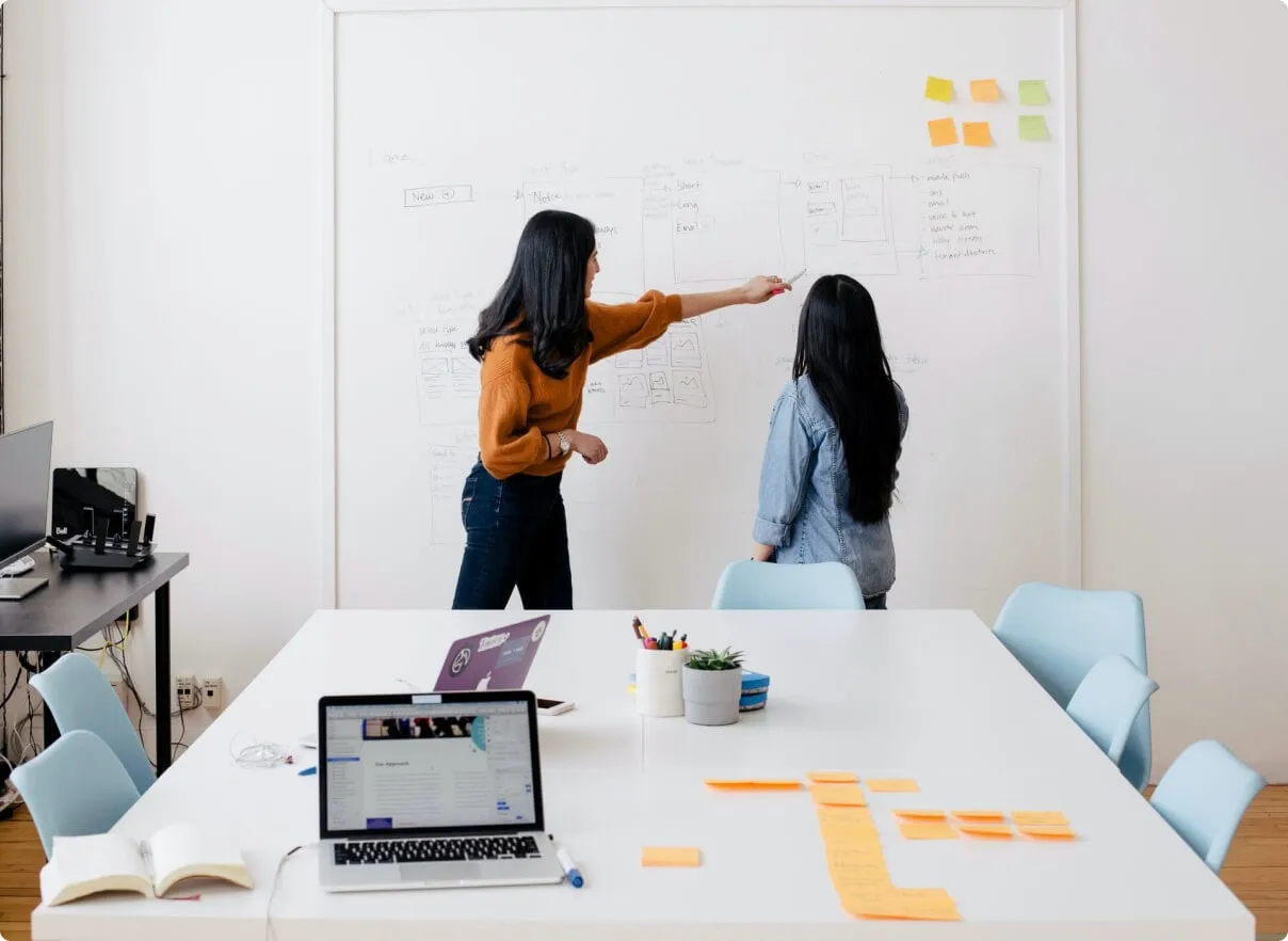 Two women planning a project on a whiteboard in a modern meeting room