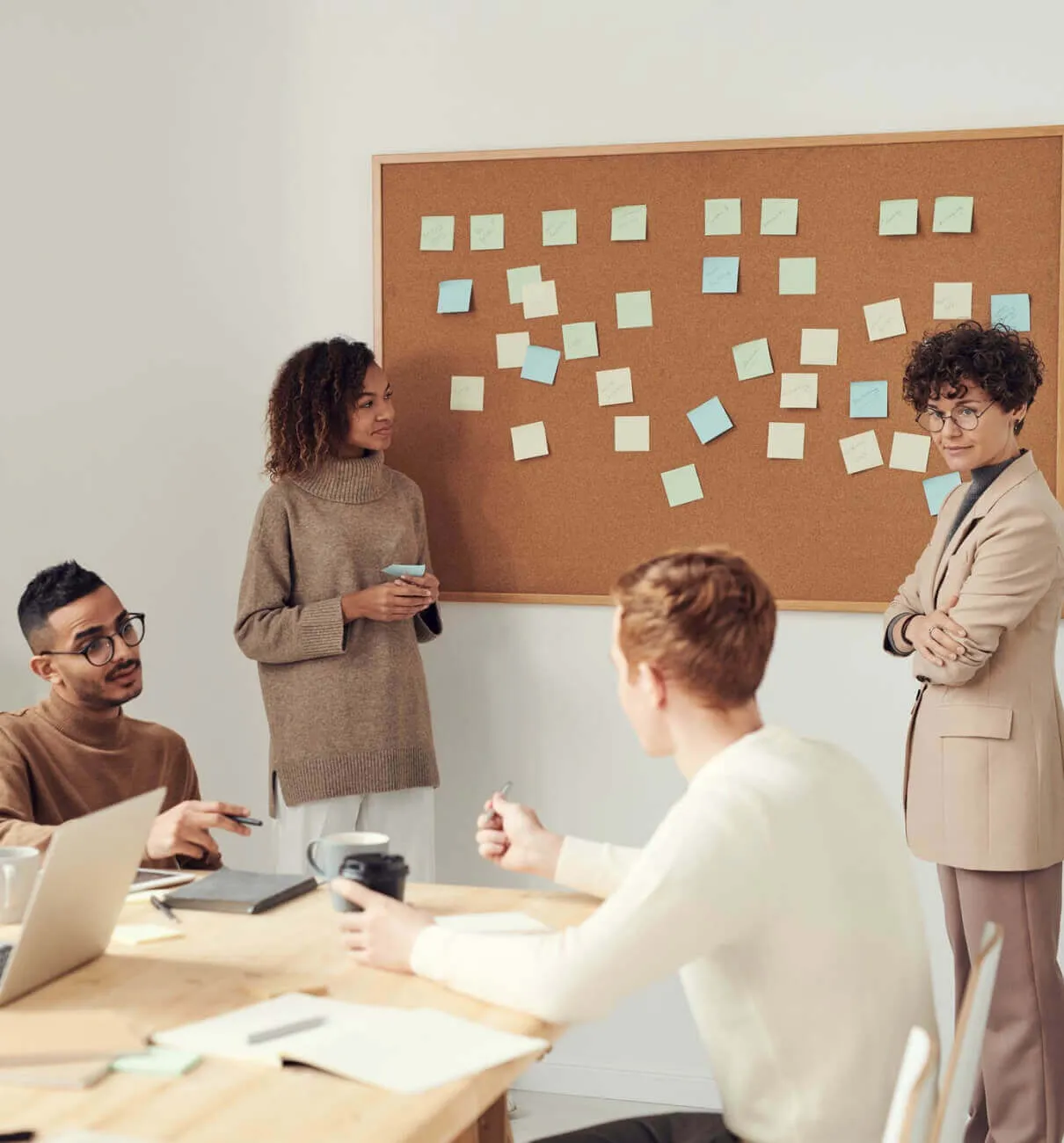 Team members discussing ideas using sticky notes on a cork board during a brainstorming session