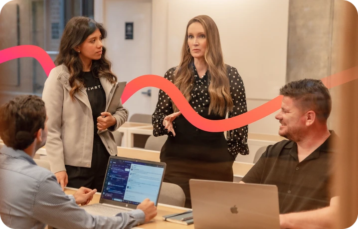 Four people in a modern office setting, engaged in discussion around a table with laptops, collaborating on Enterprise SEO Software, with a red wavy line overlaid on the image.