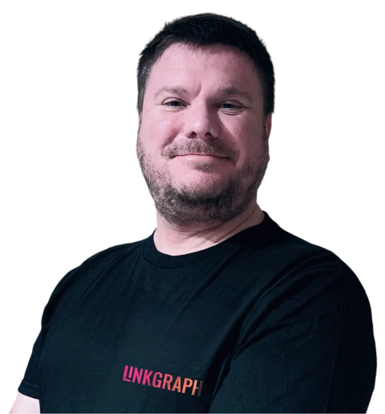 A man with short brown hair and a beard is standing with his arms crossed, wearing a black LINKGRAPH t-shirt—showcasing confidence in Enterprise SEO Software—against a plain background.